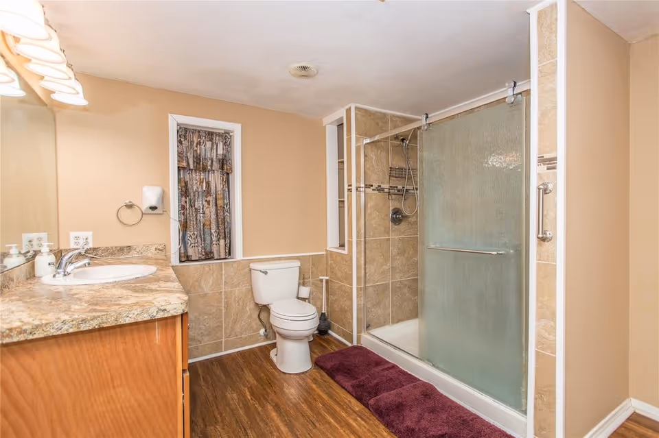 Bathroom with a vanity and sink on the left, a toilet in the center, and a tiled walk-in shower with a sliding glass door on the right.