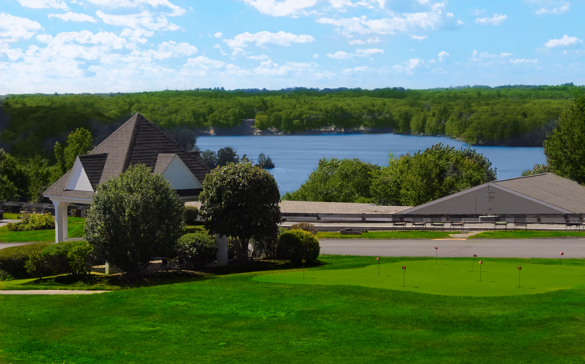 Grassy putting green and small gazebo with trees and a lake visible in the background.