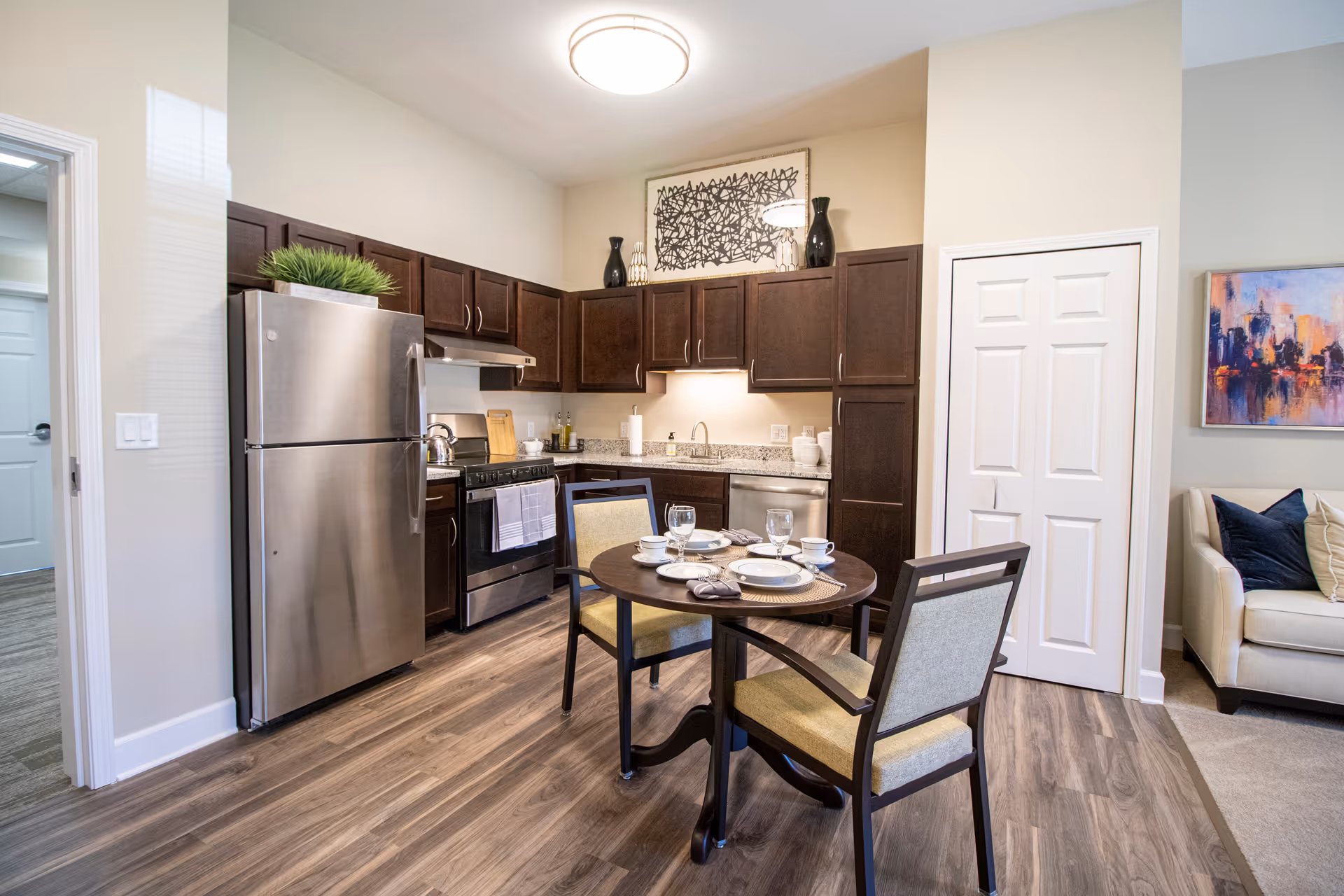 Well-lit kitchen with stainless steel refrigerator and stove, dark wood cabinets, and a small round dining table set for four.