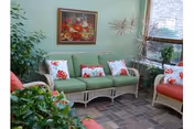 A cozy senior living lounge with green cushioned wicker sofas, red-patterned pillows, and plants.