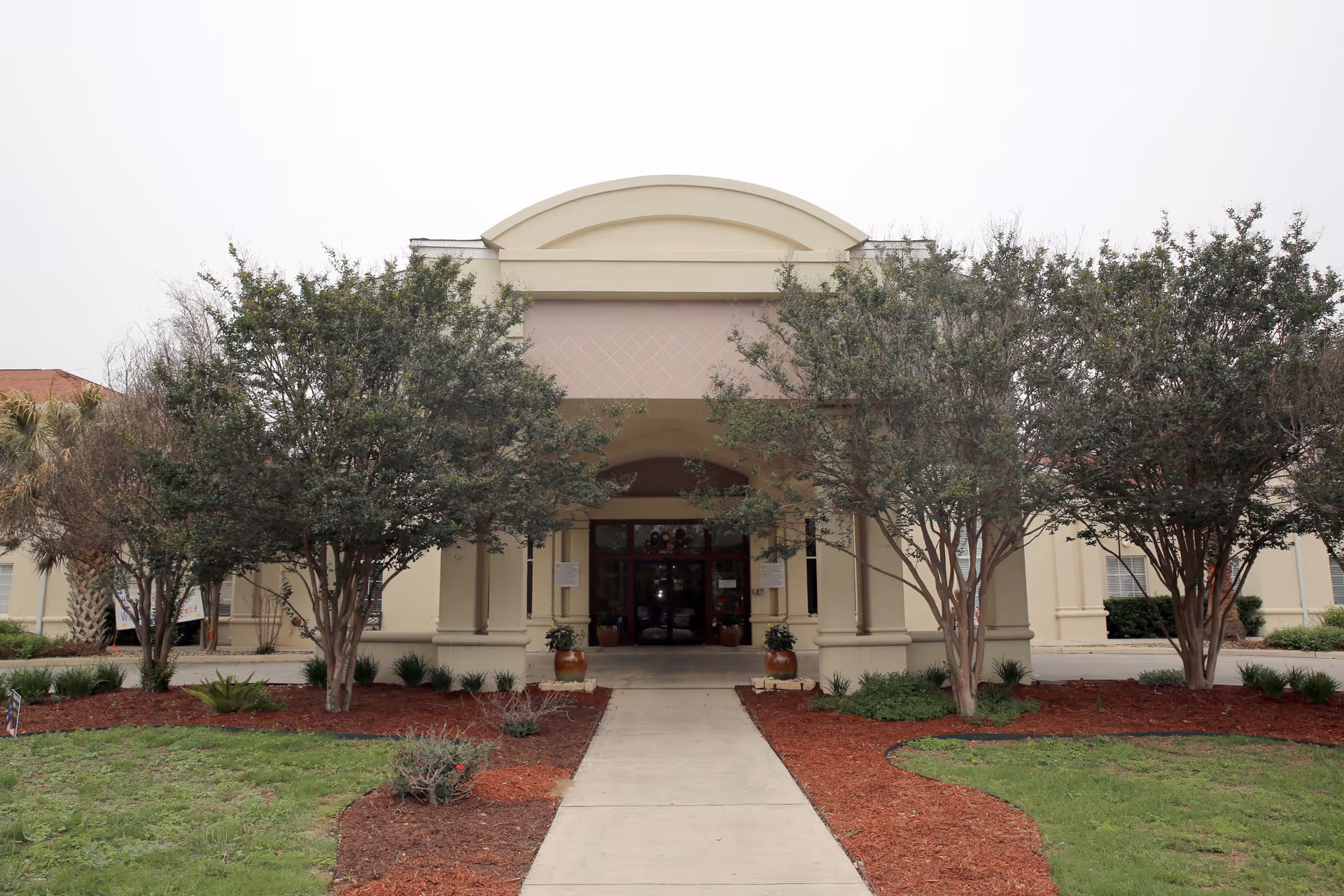 Front entrance of Esplanade Gardens senior living building with a covered entryway, walkway, and trees.