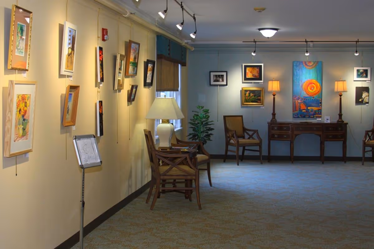 Interior common room with framed artwork on the walls, chairs, lamps, and a wooden console table.