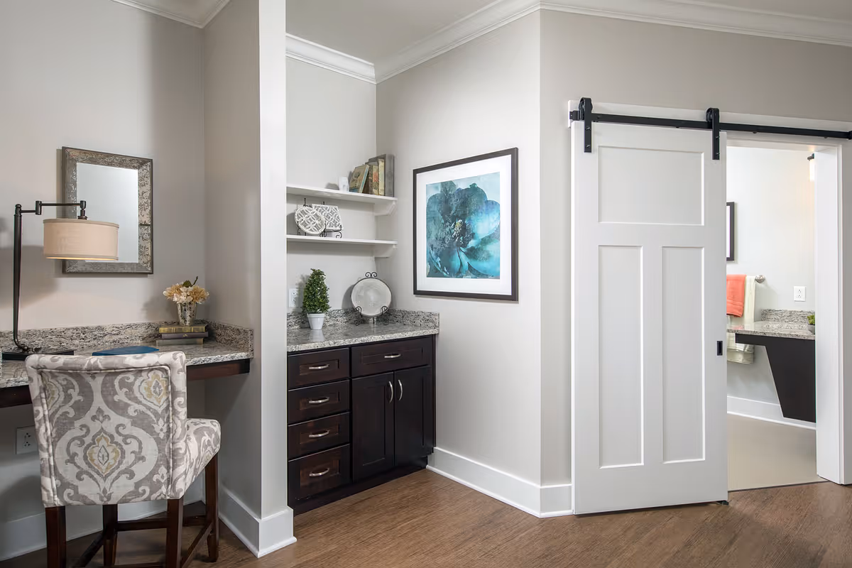 Interior living space with a patterned desk chair, granite countertop cabinets and shelves, wall art, and a white sliding barn door.