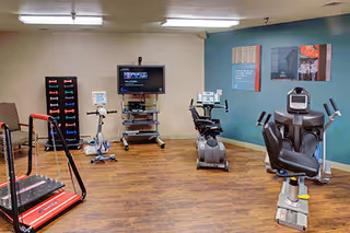 Interior exercise room with cardio machines, a TV, and a wooden floor at Marquis Vermont Hills.