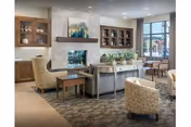 A bright senior living community lounge with armchairs, a fireplace, built-in cabinetry, and large windows.