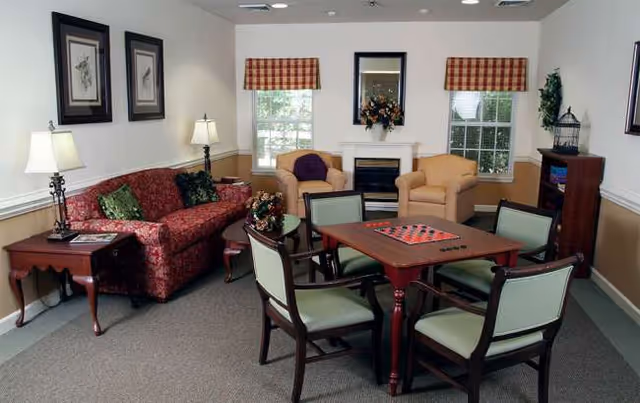 Cozy senior living lounge with sofa, chairs, and a wooden dining table.