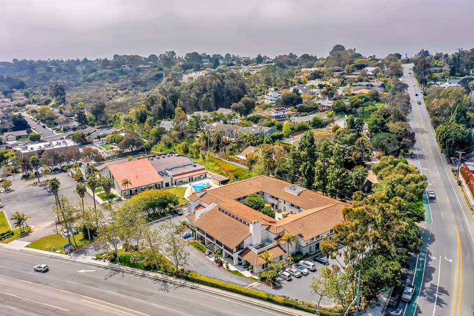 Aerial view of Encinitas Senior Living with red-tiled roofs, courtyard, pool, parking area and surrounding neighborhood.