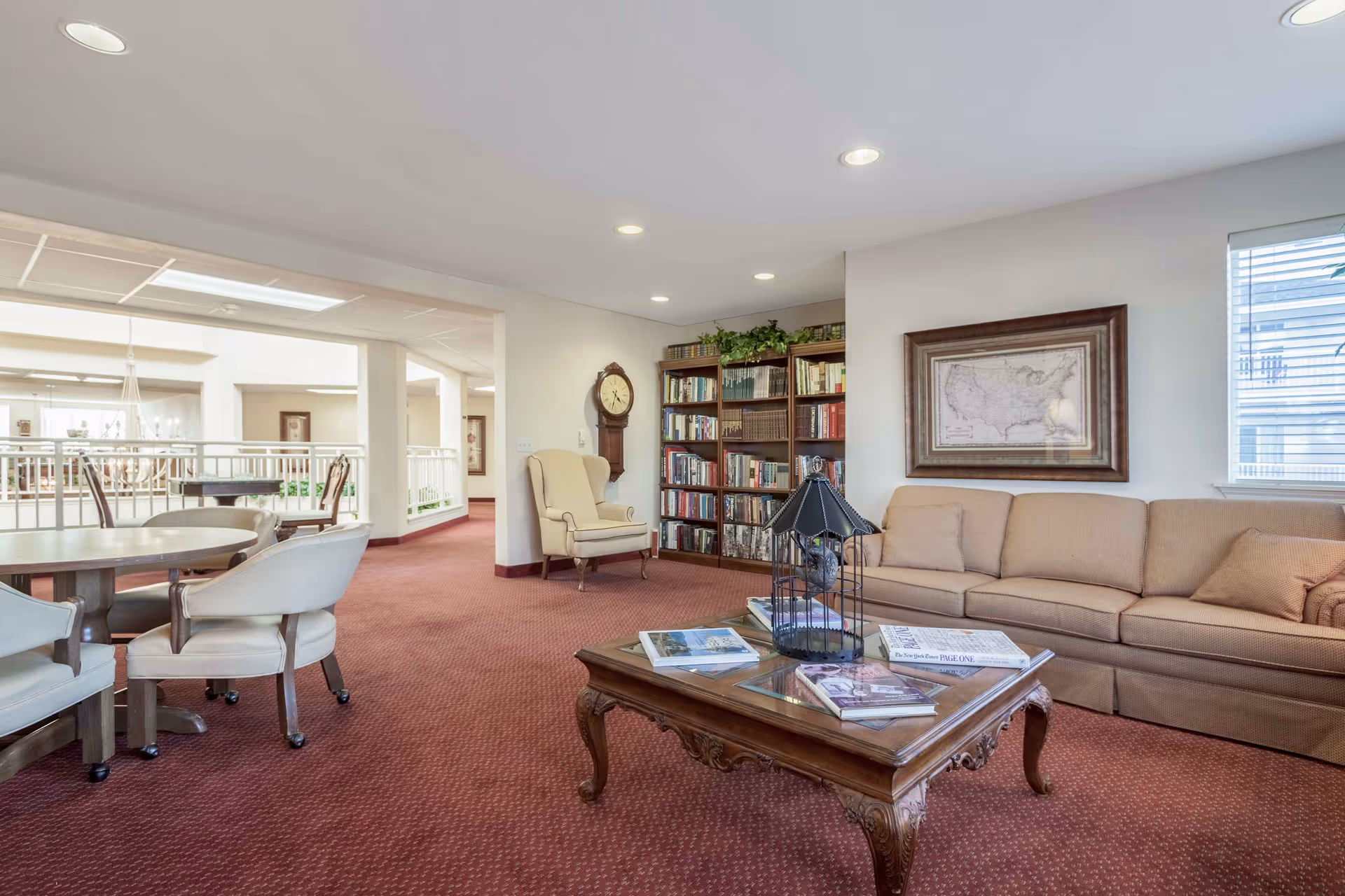 Well-lit communal living room with a sofa, coffee table, armchairs and bookshelves overlooking an open atrium.