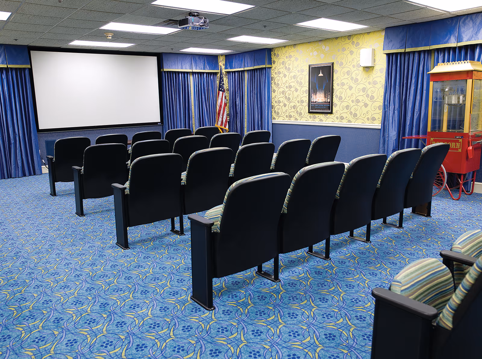 Small indoor screening room with rows of theater seats facing a large projection screen and a popcorn machine.