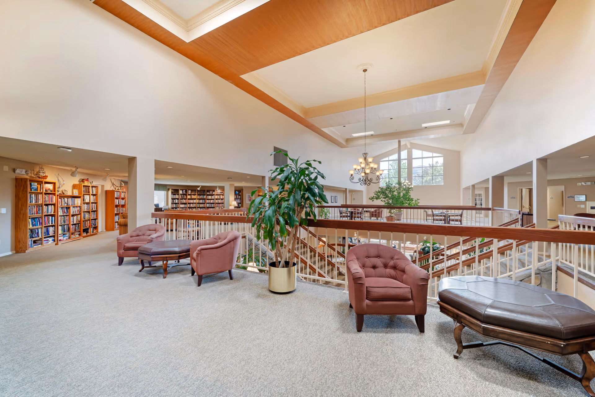 Open two-story interior common area with armchairs, bookshelves, plants and a central atrium railing.