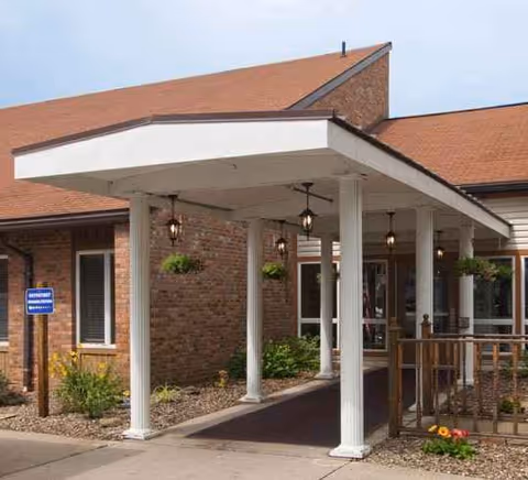 Brick building entrance with white columns, canopy, hanging plants, and ramp.