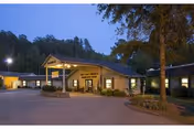 Exterior view of Perry County Nursing & Rehab Center at dusk, showing the main entrance with a covered driveway, surrounded by trees and well-lit with outdoor lights.