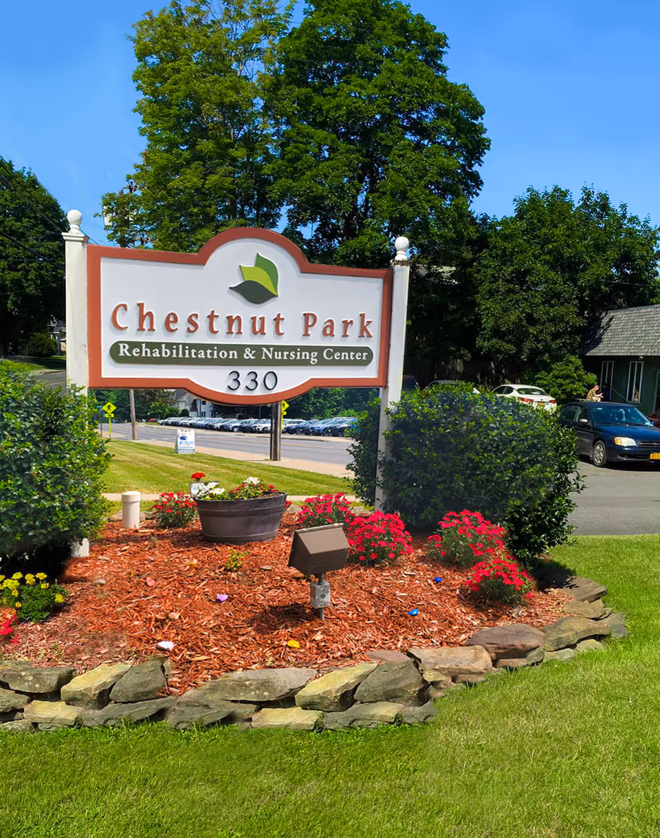 Entrance sign reading "Chestnut Park Rehabilitation & Nursing Center" with landscaping, flowers, and the address number 330 in front of the facility.