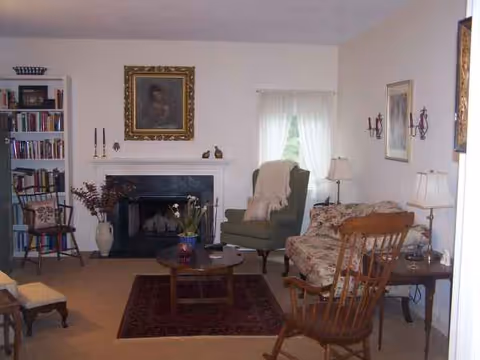 Cozy living room with seating, fireplace, bookshelf, and soft lighting in a senior facility.