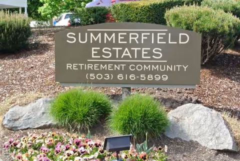 Outdoor sign for Summerfield Estates Retirement Community amid rocks, shrubs, and flowers.