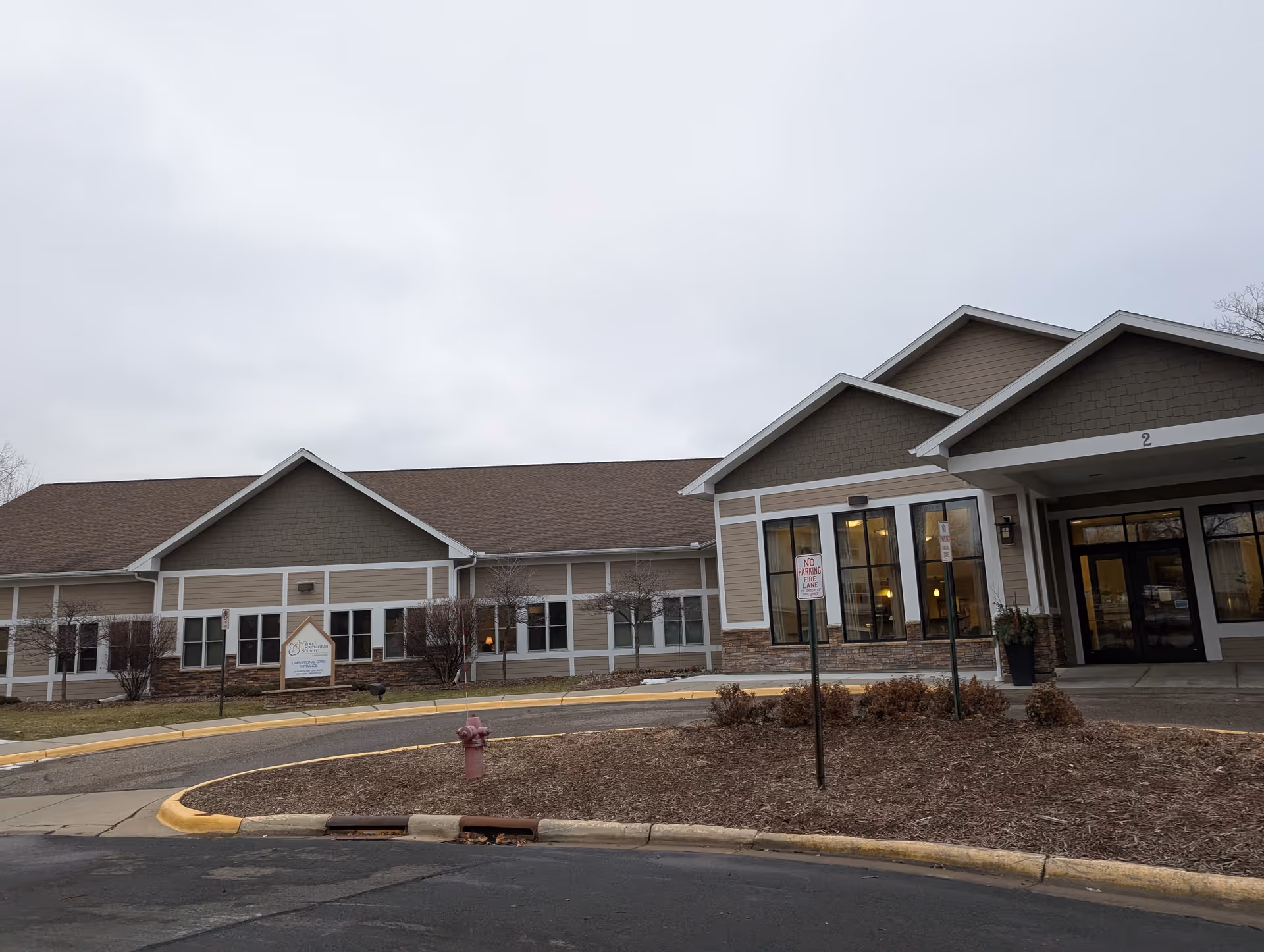 Front exterior of a one-story senior living facility showing a covered entrance, windows, and a circular driveway with landscaping.