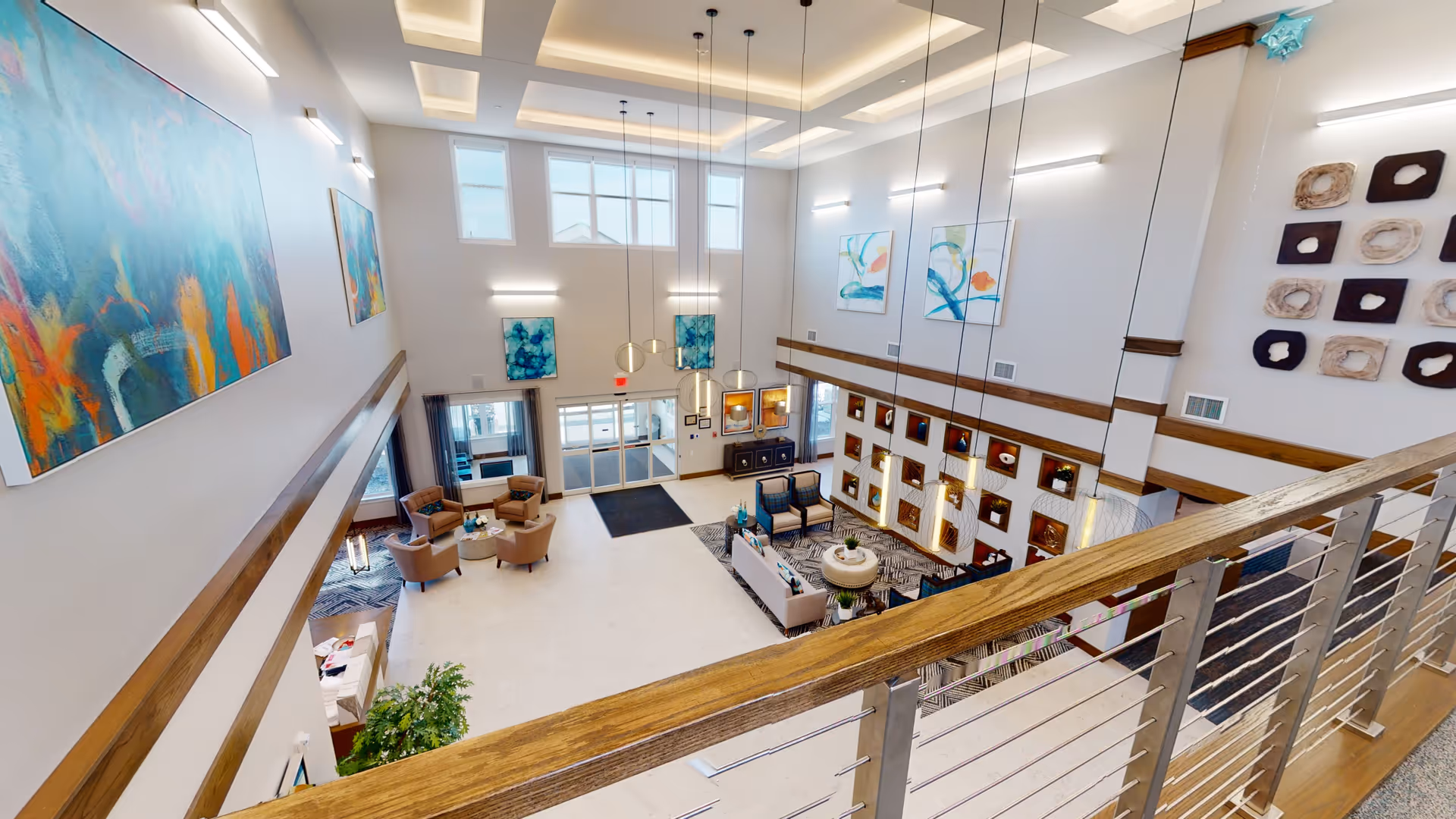 Spacious two-story senior living lobby with seating areas, colorful wall art, and a balcony railing overlooking the reception area.