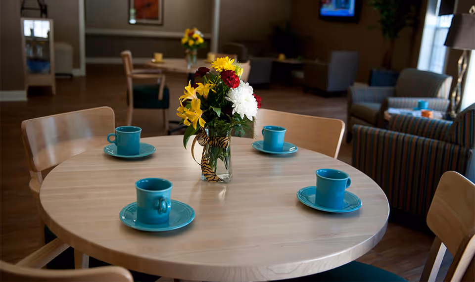 Round wooden table set with a vase of flowers and four turquoise cups and saucers in a communal lounge.