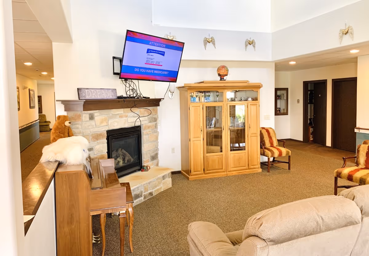 Cozy indoor lounge with fireplace, mounted TV, wooden cabinet, and cushioned seating.