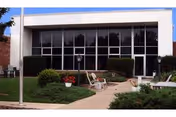 A senior living facility exterior with large glass windows and outdoor seating area.