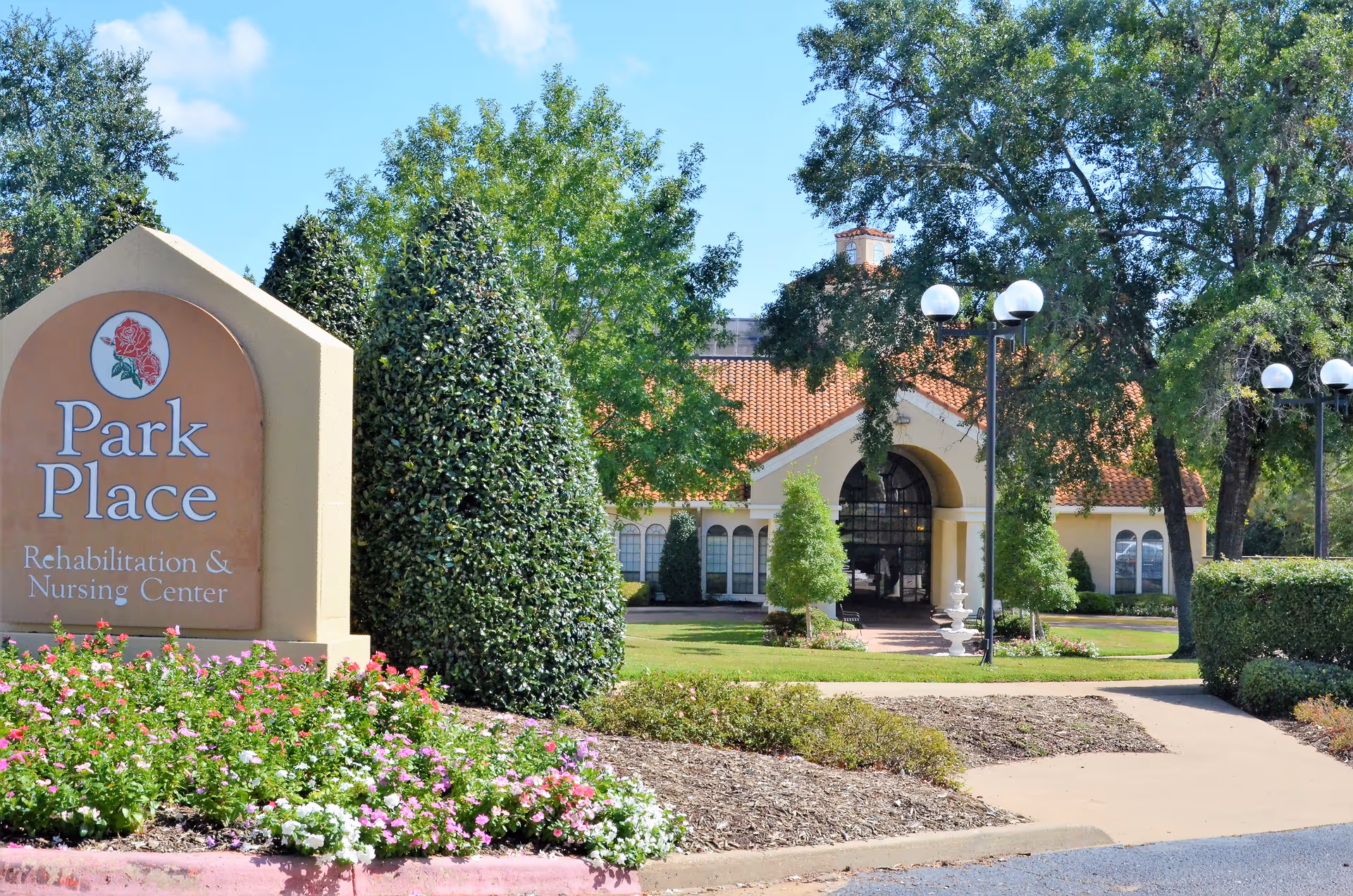 Front entrance of Park Place Rehabilitation & Nursing Center with its sign, landscaped flowerbeds, and an arched building façade.