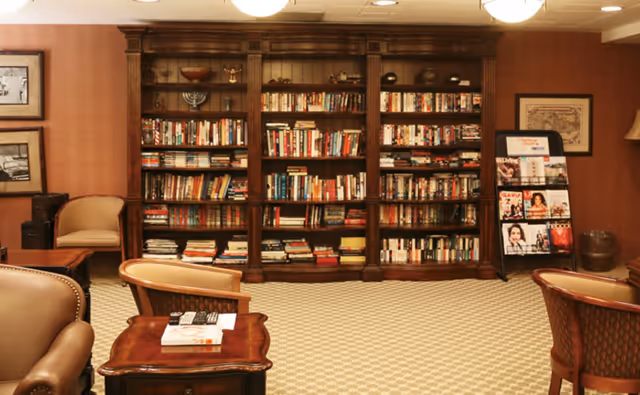 Cozy lounge with a large wooden bookshelf filled with books, upholstered chairs, side tables, and a magazine rack.