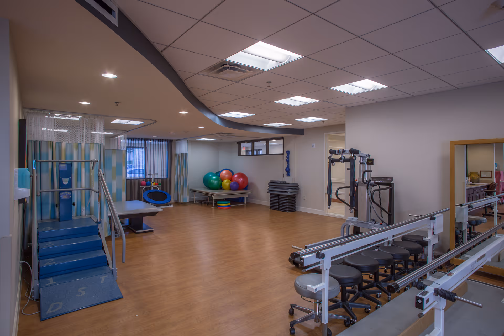 Indoor rehabilitation/fitness room with therapy stairs, parallel bars, exercise equipment and colorful stability balls.