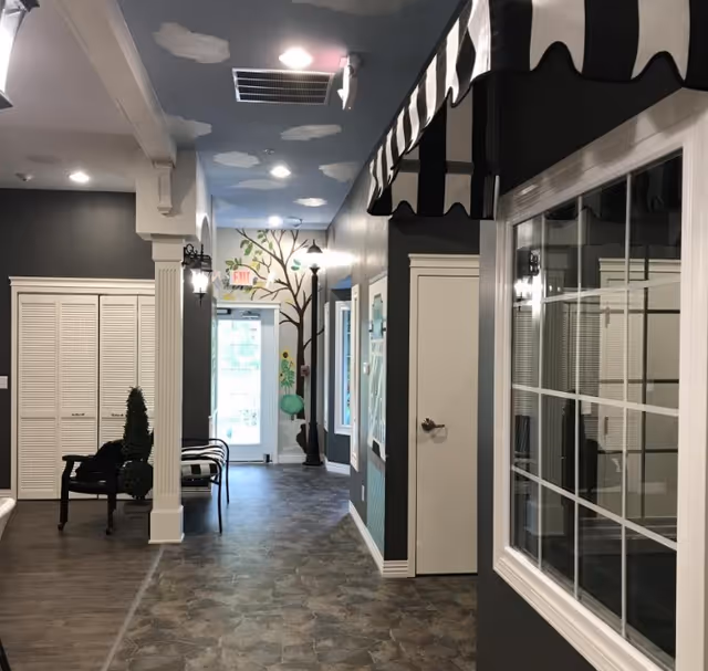 Interior hallway with seating, decorative ceiling clouds, a painted tree mural at the far end, and a black-and-white striped awning over a window.