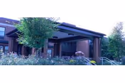 Covered entrance and portico of a brick senior living building with steps, a ramp, and surrounding landscaping.