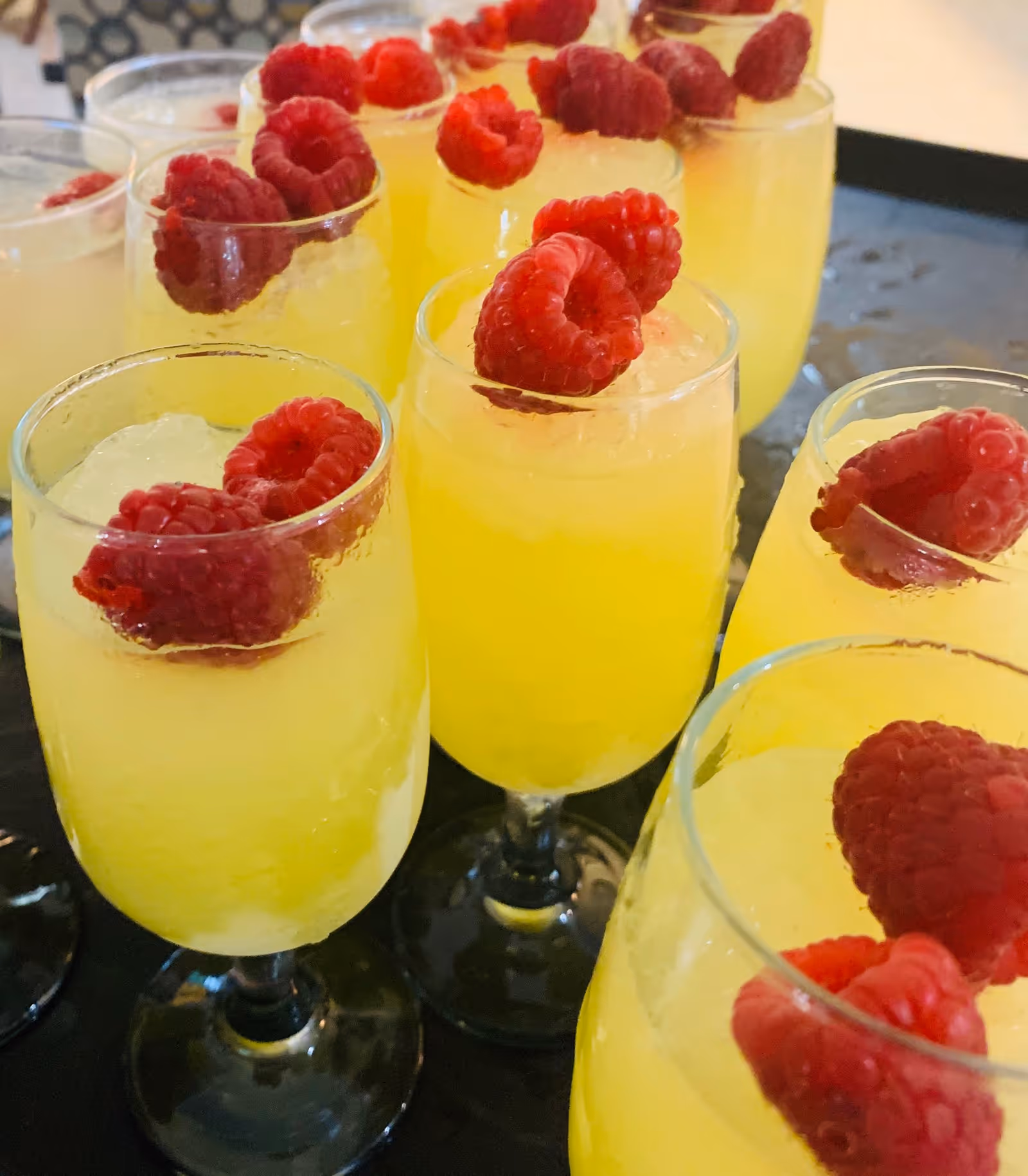 Close-up of yellow beverages in stemmed glasses each topped with a raspberry.