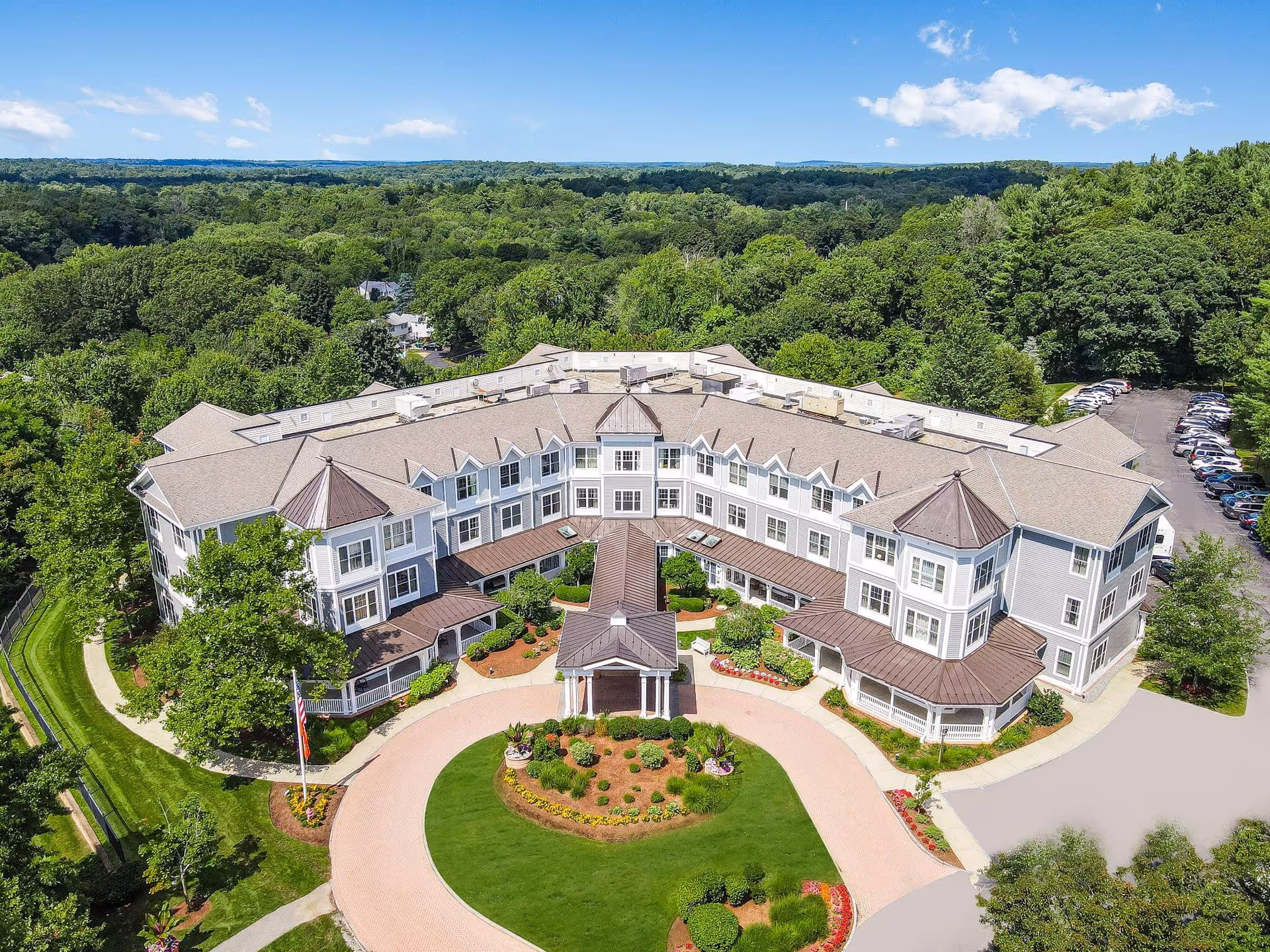 Aerial view of a large senior living building with a circular driveway, landscaped entrance, and surrounding trees.