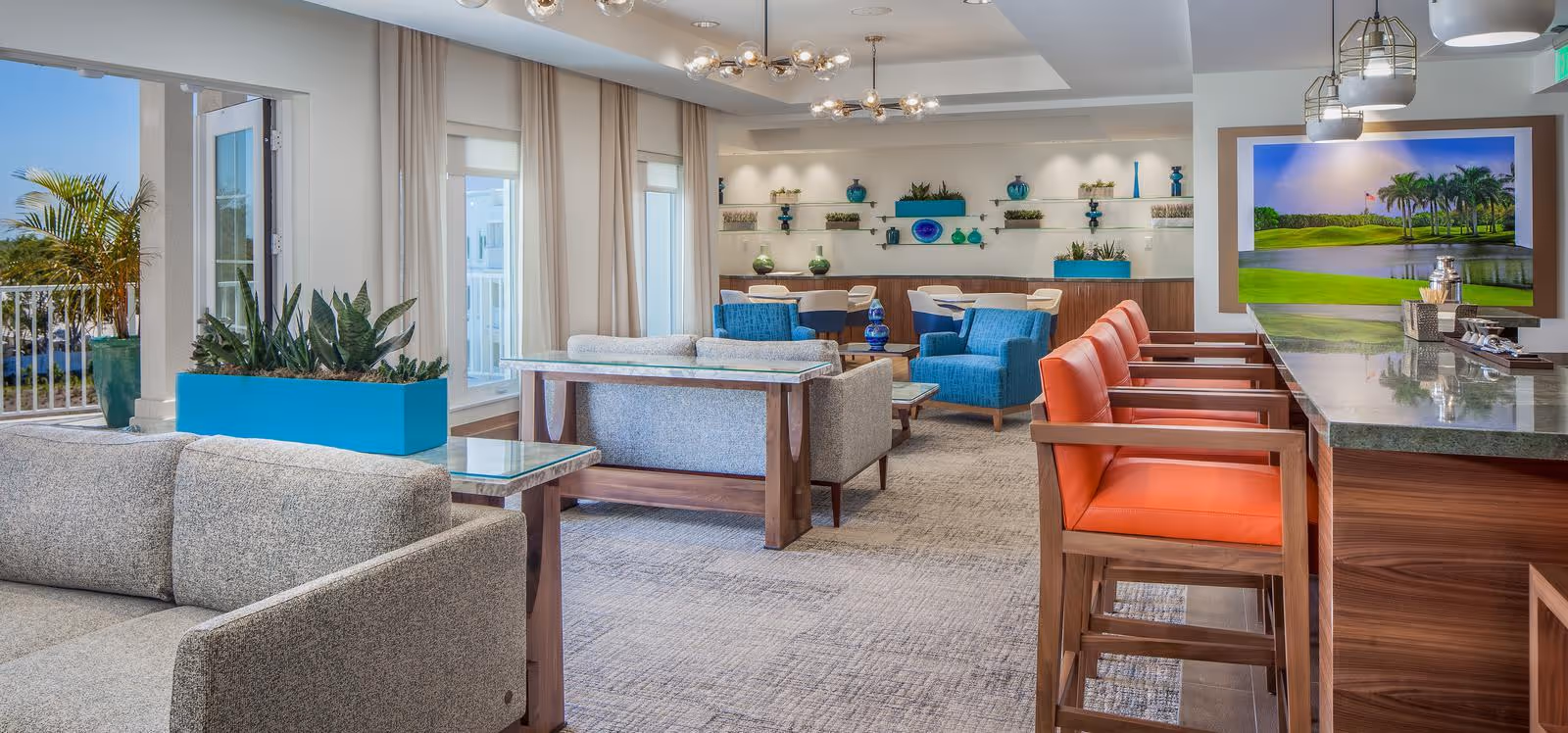 Bright, modern common lounge with sofas, blue and orange seating, a bar counter with stools, plants, and a large TV displaying a golf course.