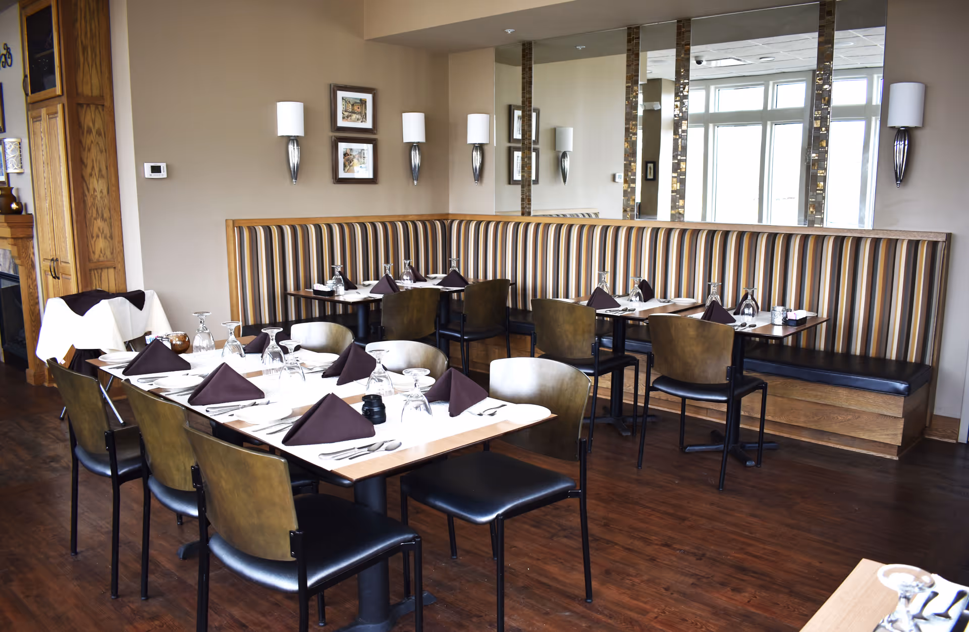 Dining area with set tables, striped banquette seating, chairs, and folded napkins at place settings.