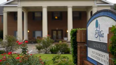 Front entrance of a senior living facility with a brick sign and columns.