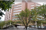 Brick multi-story building with trees in foreground and a visible entrance.