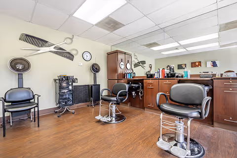 Small salon interior with barber chairs, mirrors, a hair-washing sink, and styling stations.