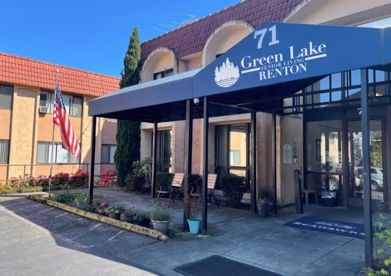 Front entrance canopy of Green Lake Senior Living Renton with seating, potted plants, and an American flag.