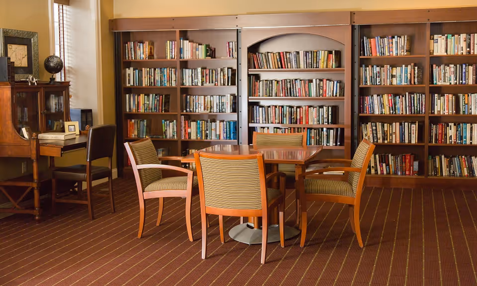 A cozy reading room with wooden bookshelves along the back wall and a round table surrounded by four chairs.