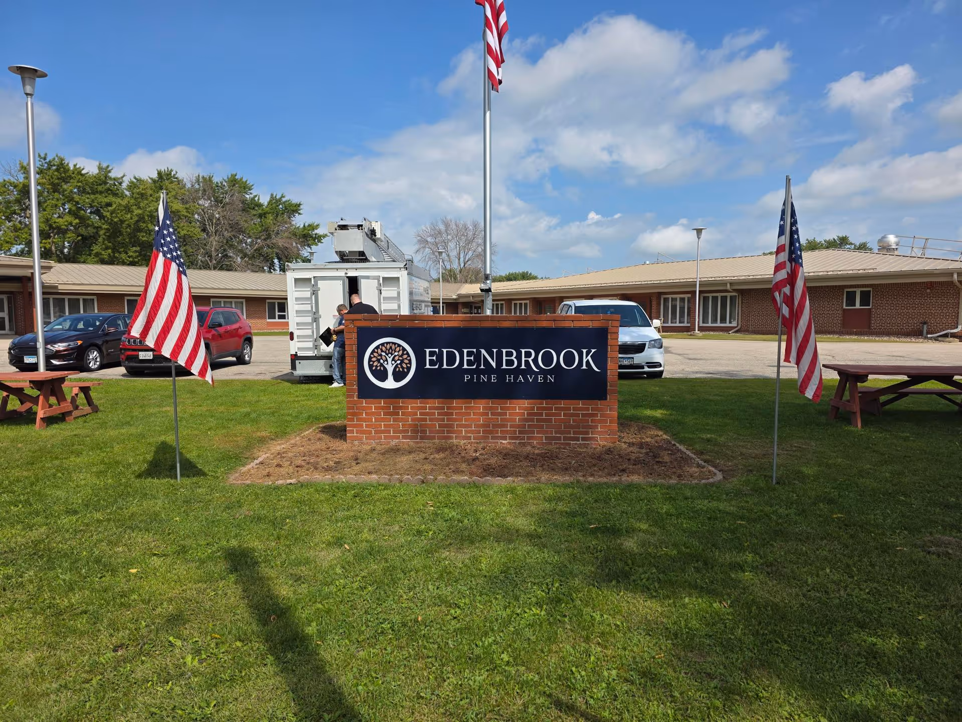 Sign for Edenbrook Pine Haven surrounded by American flags and grassy area.