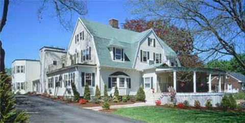 White, multi-story nursing home with a green roof and wraparound porch.