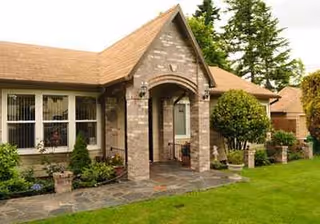 Entrance to a brick senior living facility with archway, walkway, and manicured lawn.