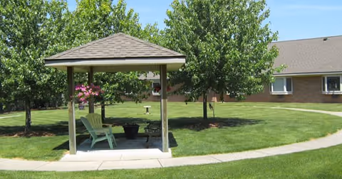 Small covered gazebo with chairs on a grassy courtyard and a brick building in the background.