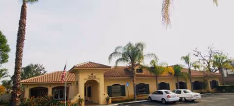 Single-story beige Brookdale Corona building with red-tiled roof and palm trees in front.