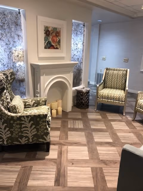 Cozy lounge with patterned armchairs, a decorative white mantel with candles, side tables and parquet-style flooring.