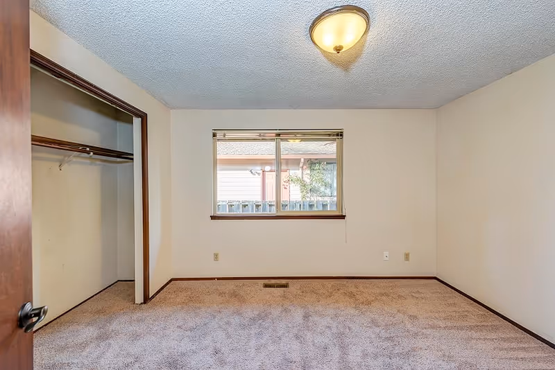 Empty carpeted bedroom with an open closet, a single window, and a ceiling light fixture.