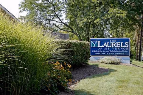 Blue sign for The Laurels of Mt. Vernon beside shrubs and trees.