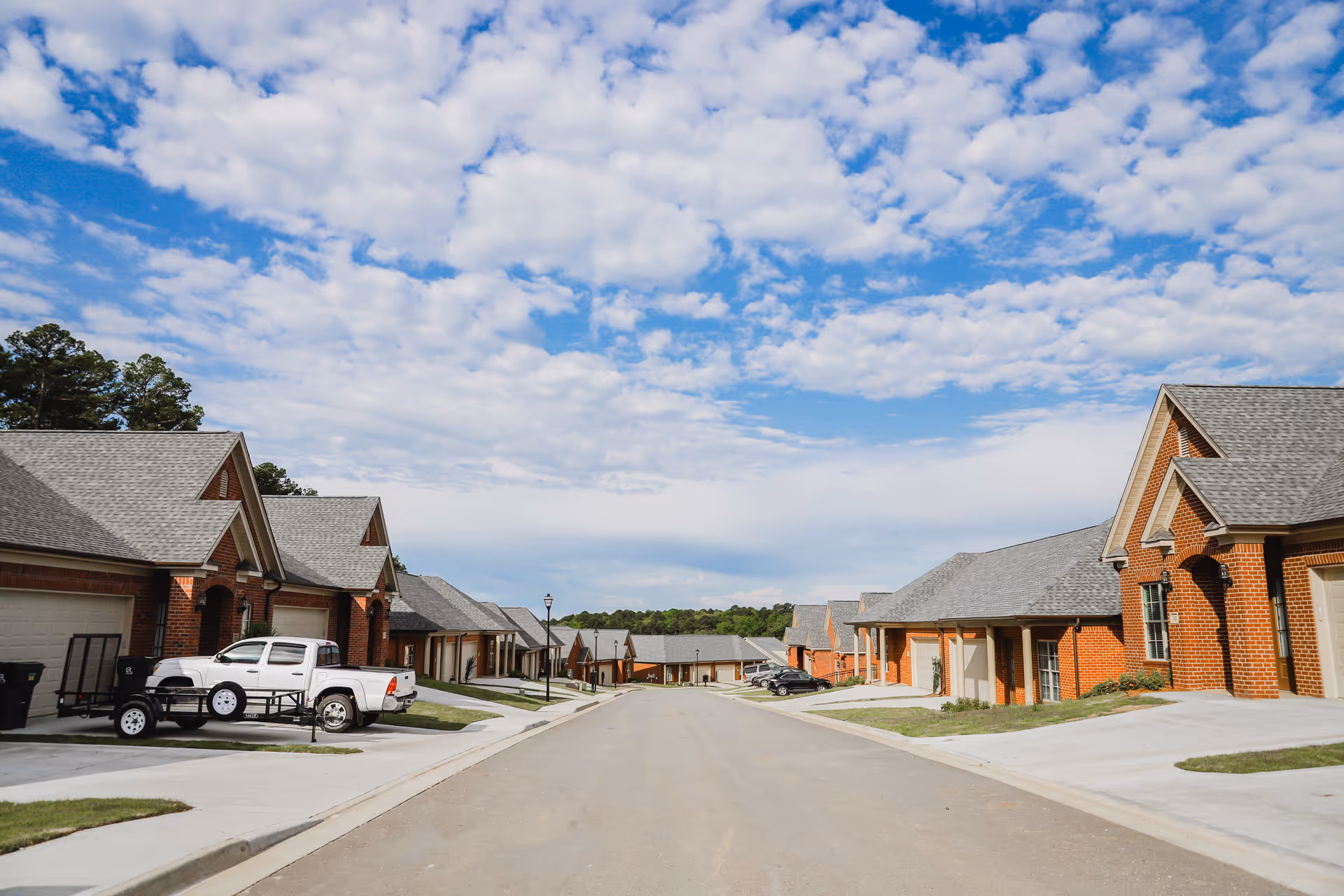 A quiet street lined with single-story brick homes and garages under a partly cloudy sky.