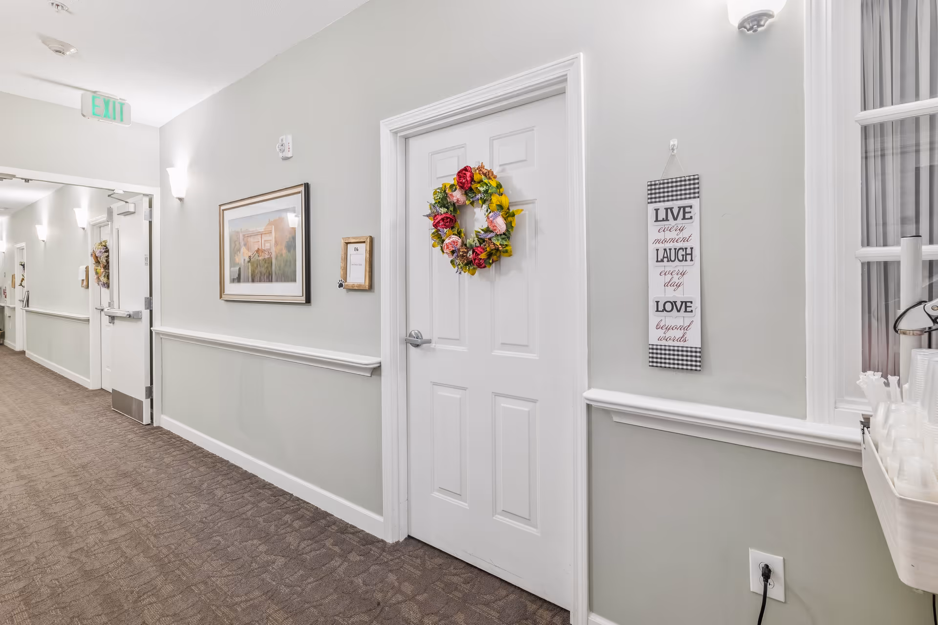 Interior hallway with a white door decorated with a floral wreath, wall art, and carpeting.