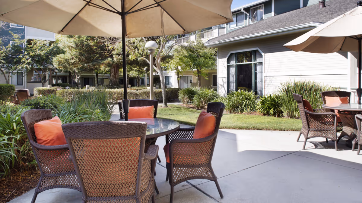 Courtyard patio with wicker tables and chairs under umbrellas outside a senior living building.