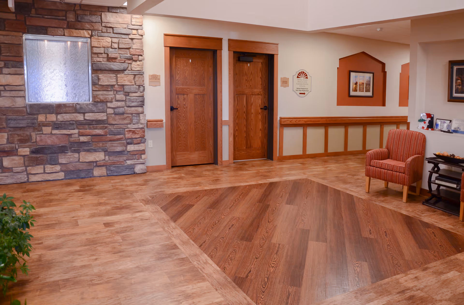 Lobby/common area with wood floors, a stone accent wall, two wooden doors and a striped armchair near a small table.